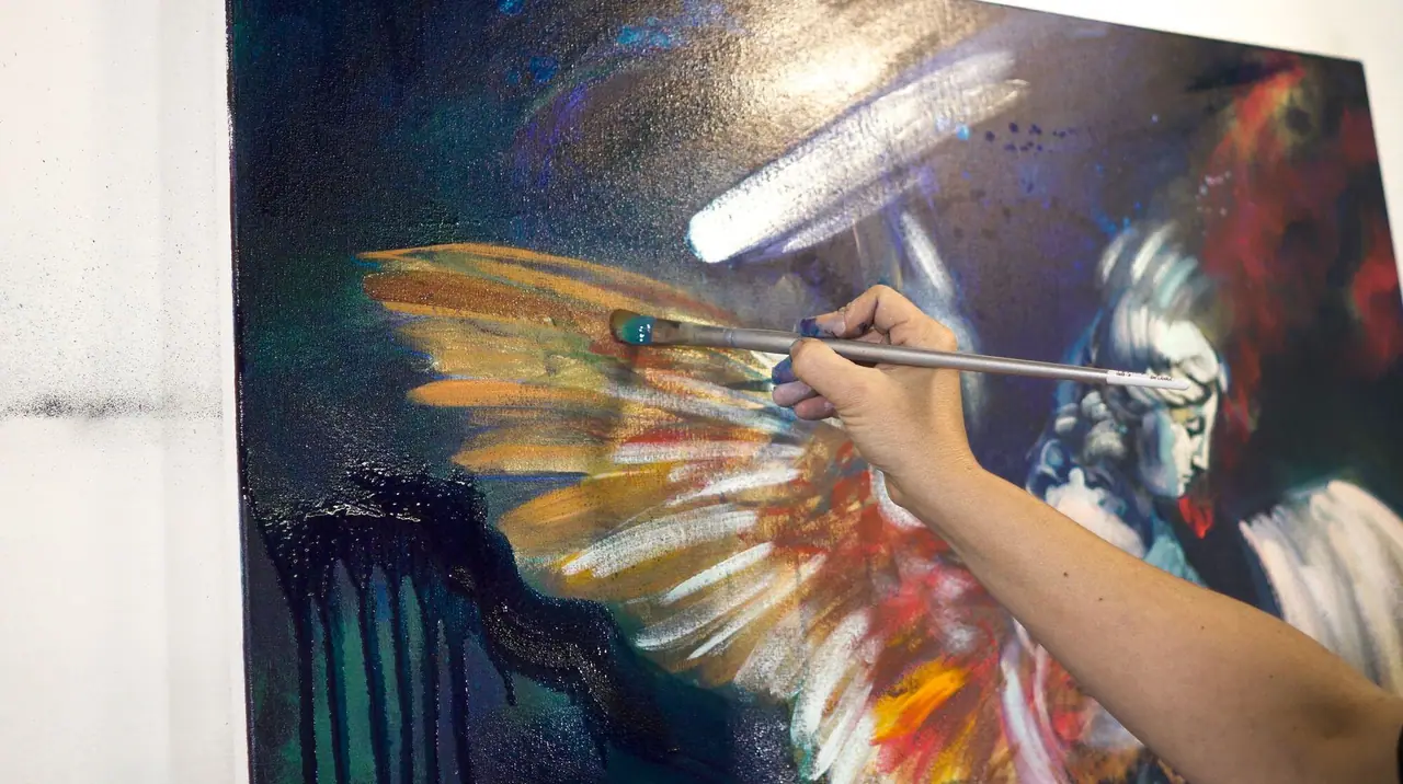 Elli Milan painting gold angel wings with red accents on a blue background
