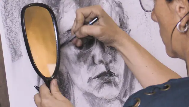 Woman drawing a portrait while holding a small mirror to see her own face