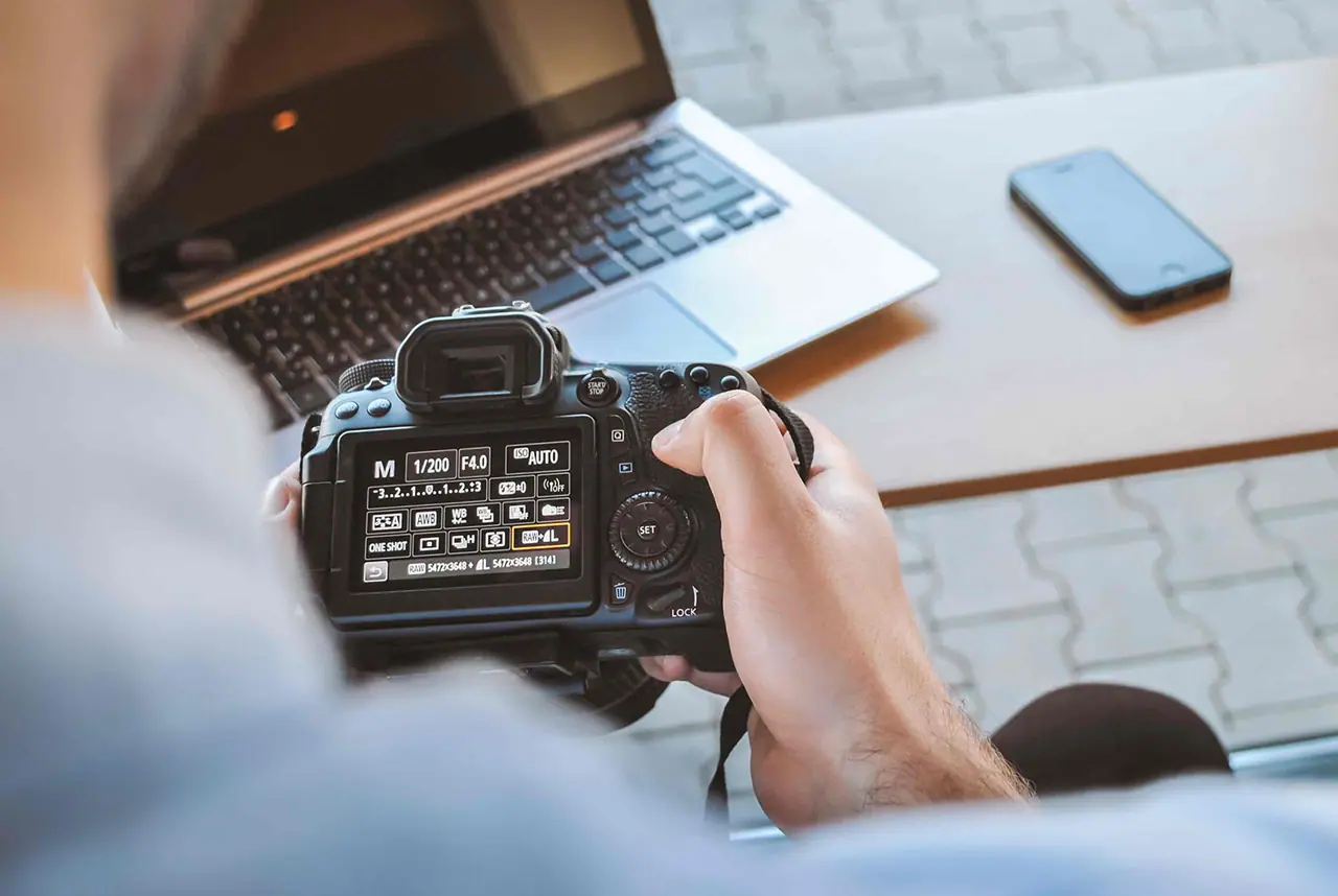 Hands adjusting a DSLR camera at a desk beside a laptop