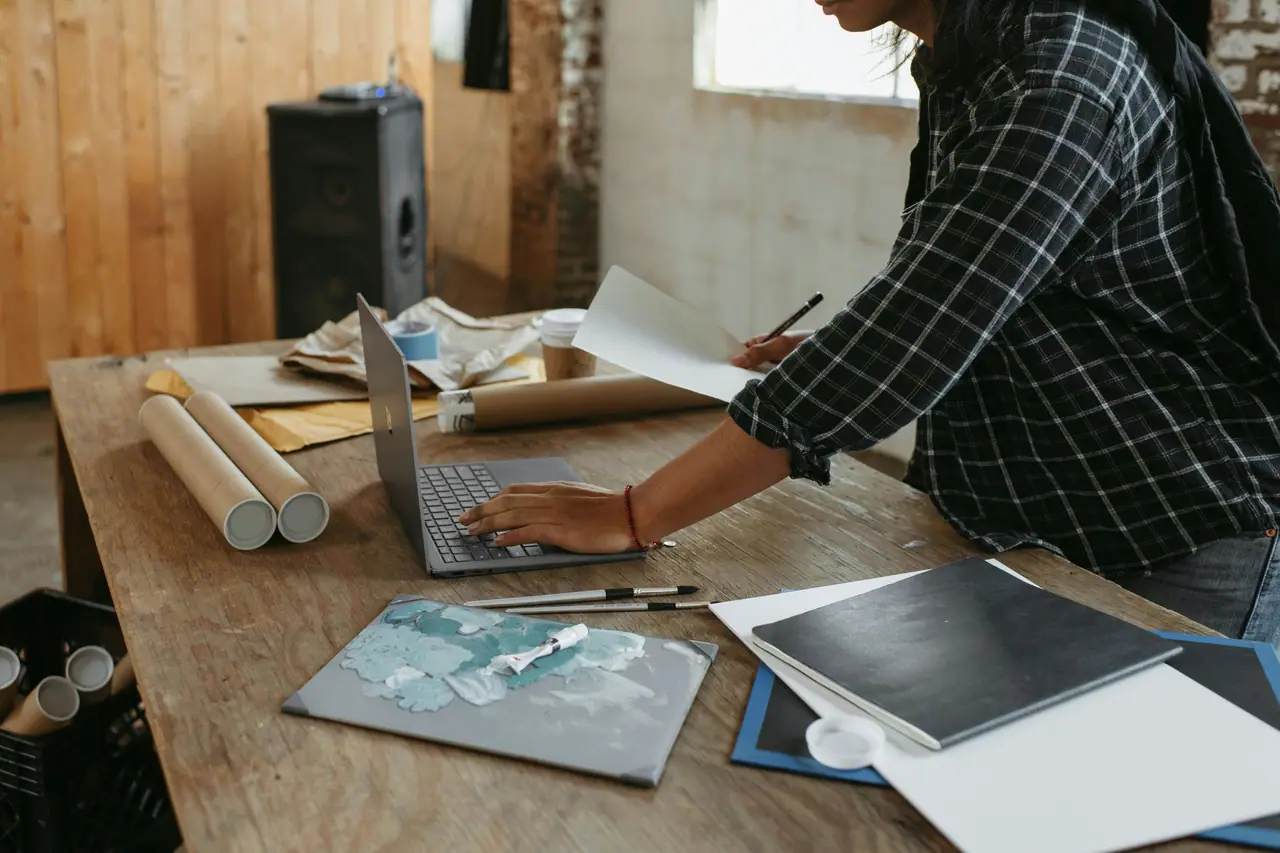Artist at a desk with a laptop preparing art prints to mail out to a collector