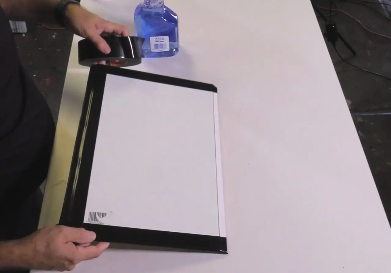 Hands wrapping solid neutral duct tape around the edges of a glass paint palette