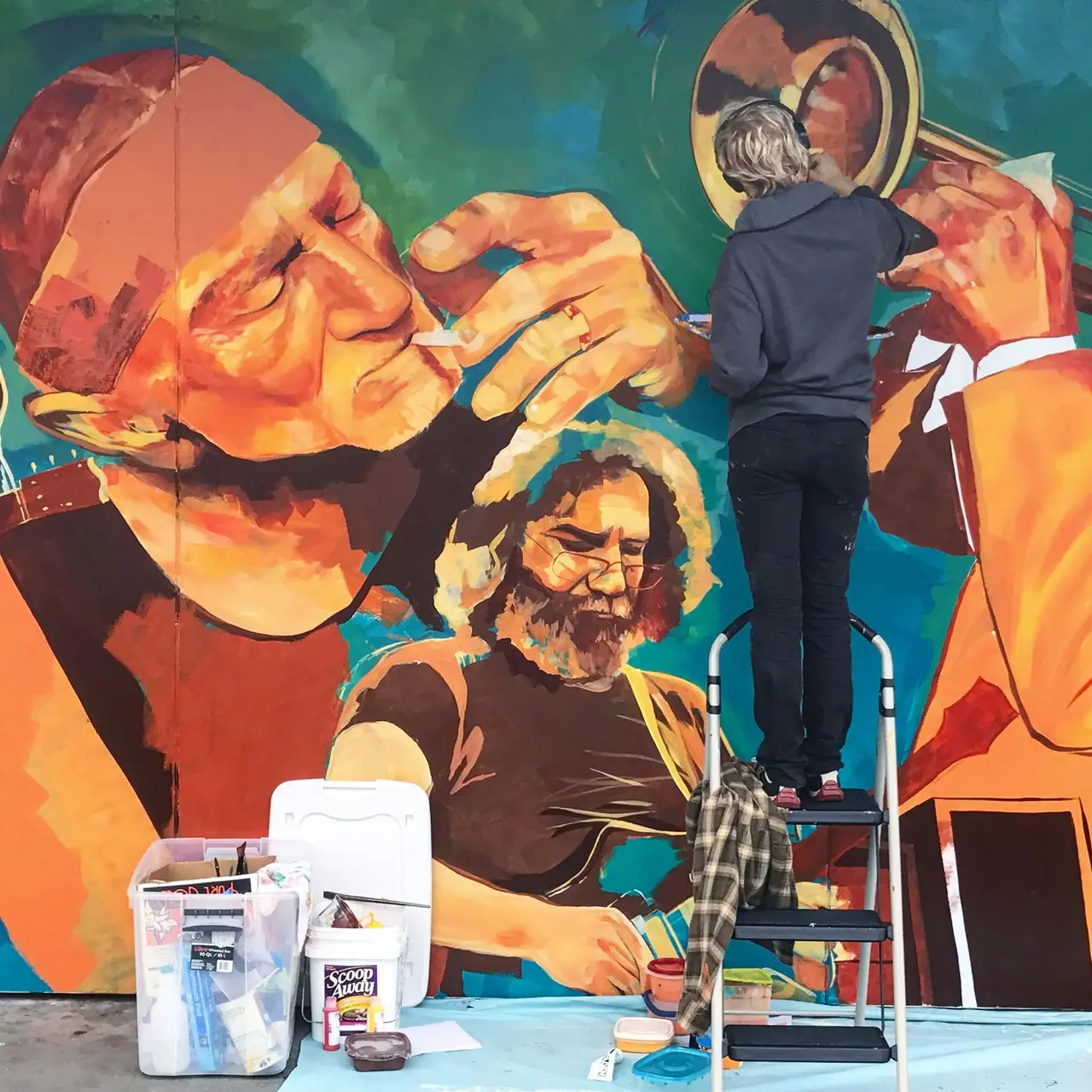 Street artist painting a colorful urban mural of musicians in blue, teal, orange, and yellow
