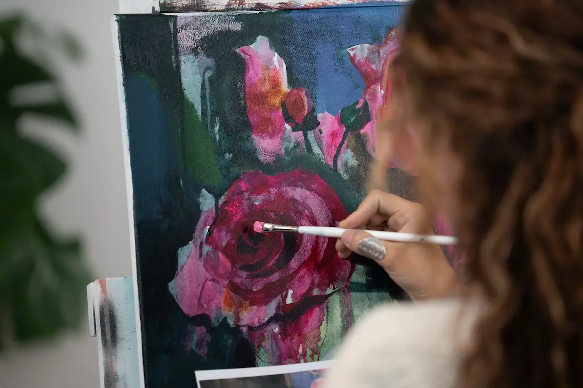 Artist painting pink flowers on canvas with a white handled oil brush