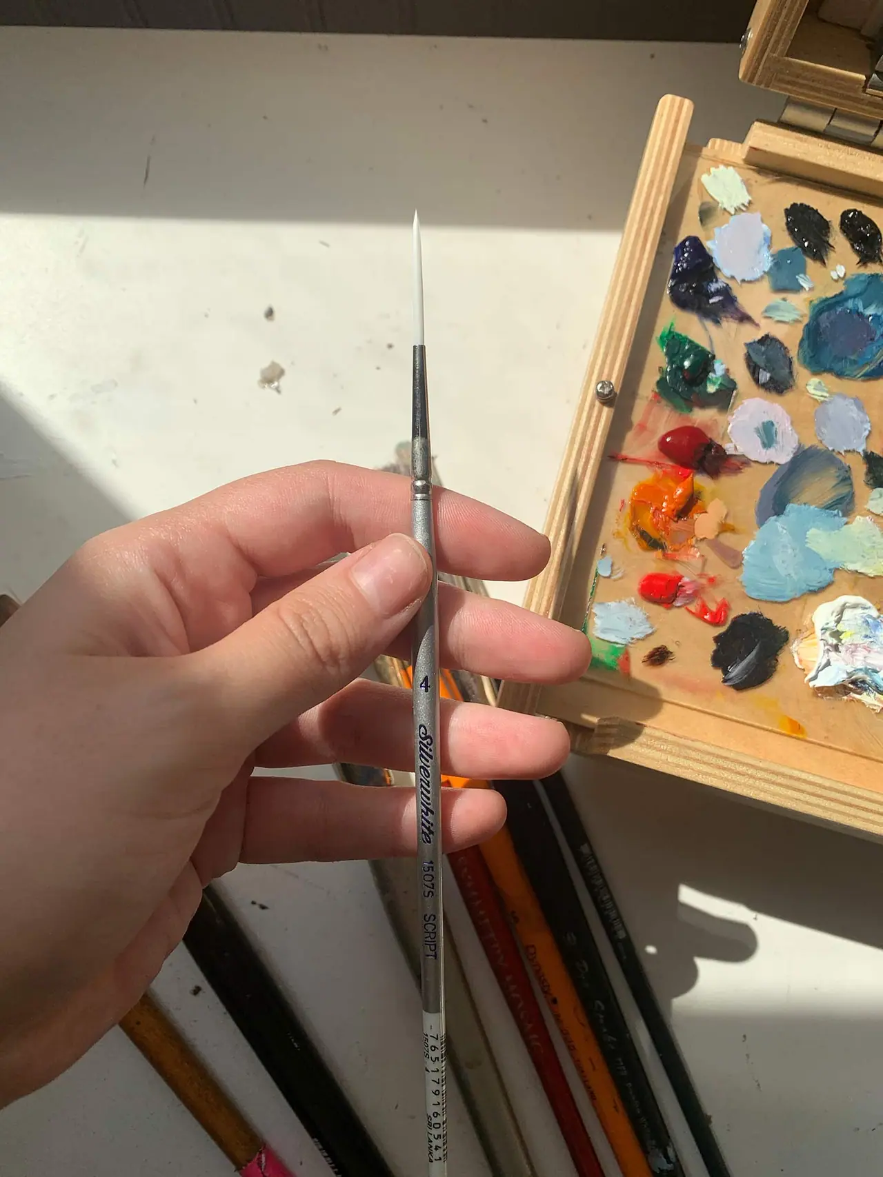 A hand holding a size 4 round artist paint brush