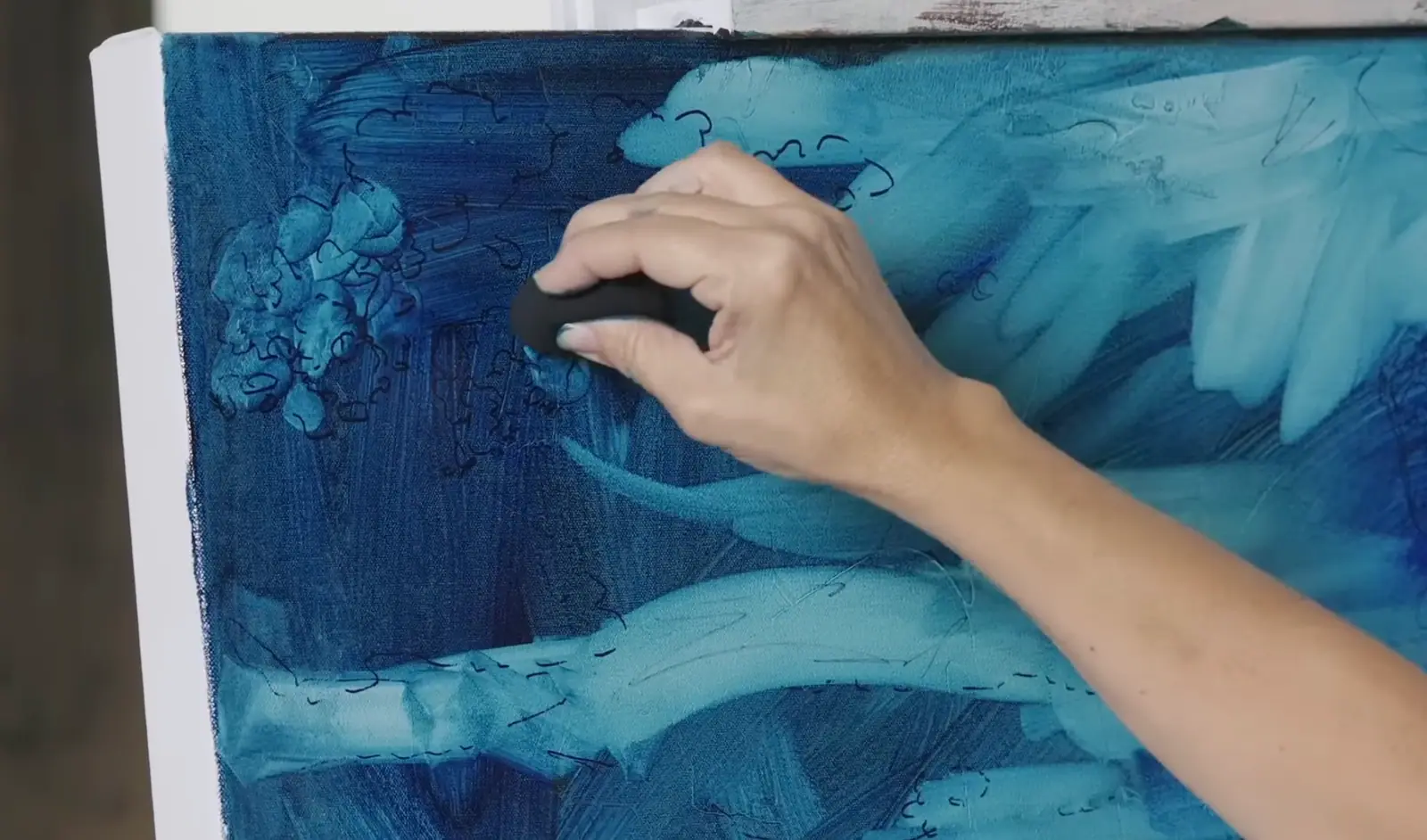 Hand lifting blue oil paint away from a canvas to reveal light