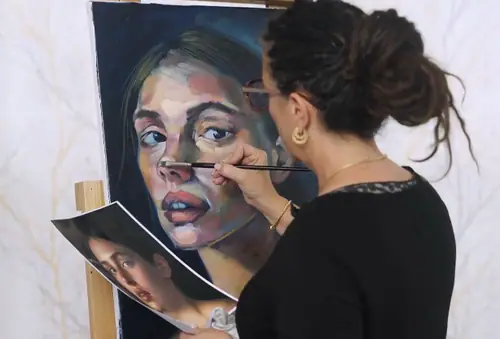 Artist painting a warm toned acrylic portrait of a woman at an easel