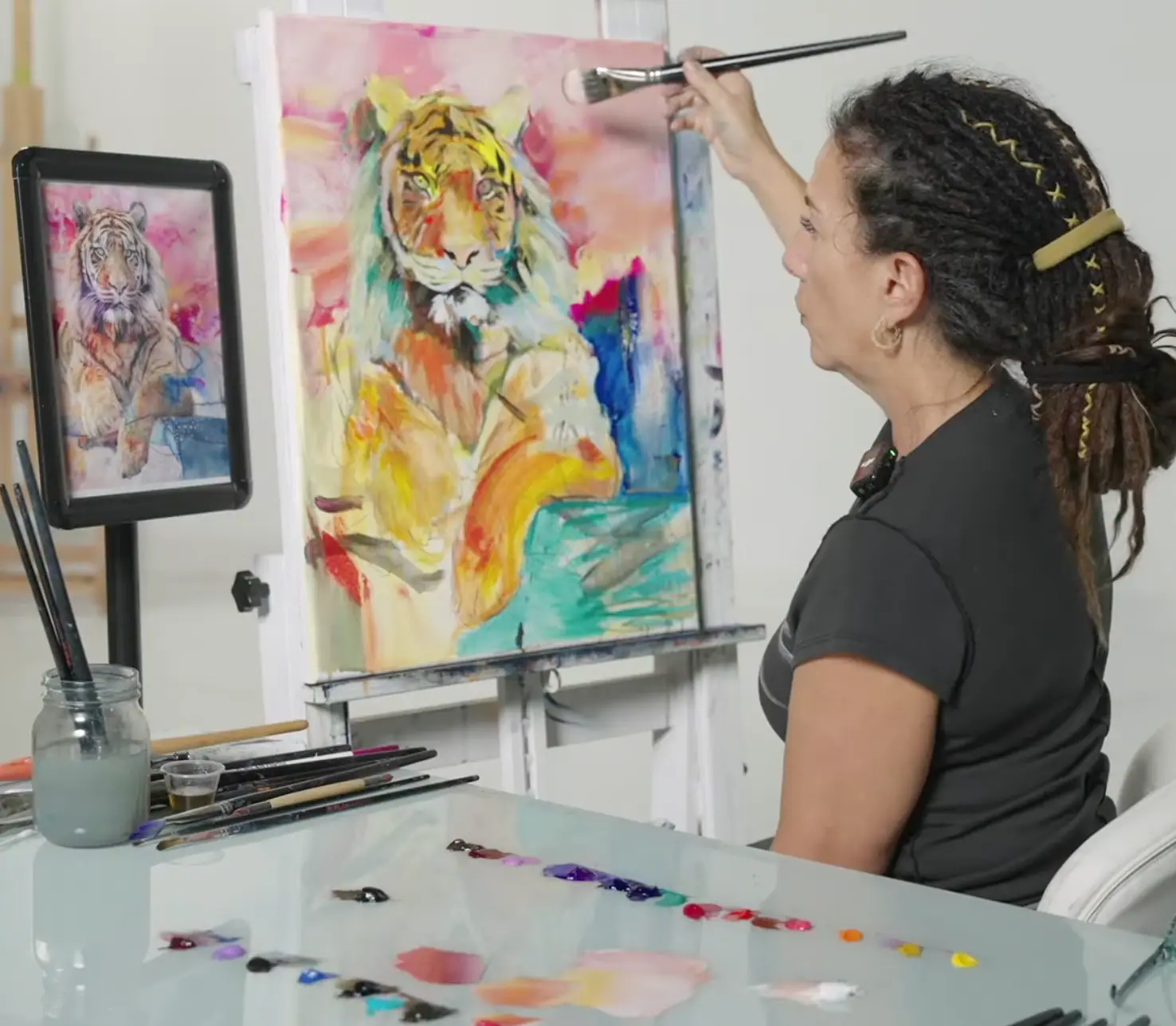 Artist painting a yellow tiger on canvas against a blue, green, and pink background