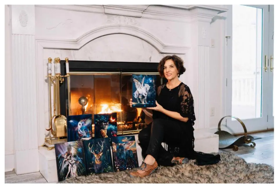 Artist holding a blue and black horse painting in front of a fire, part of a unified series
