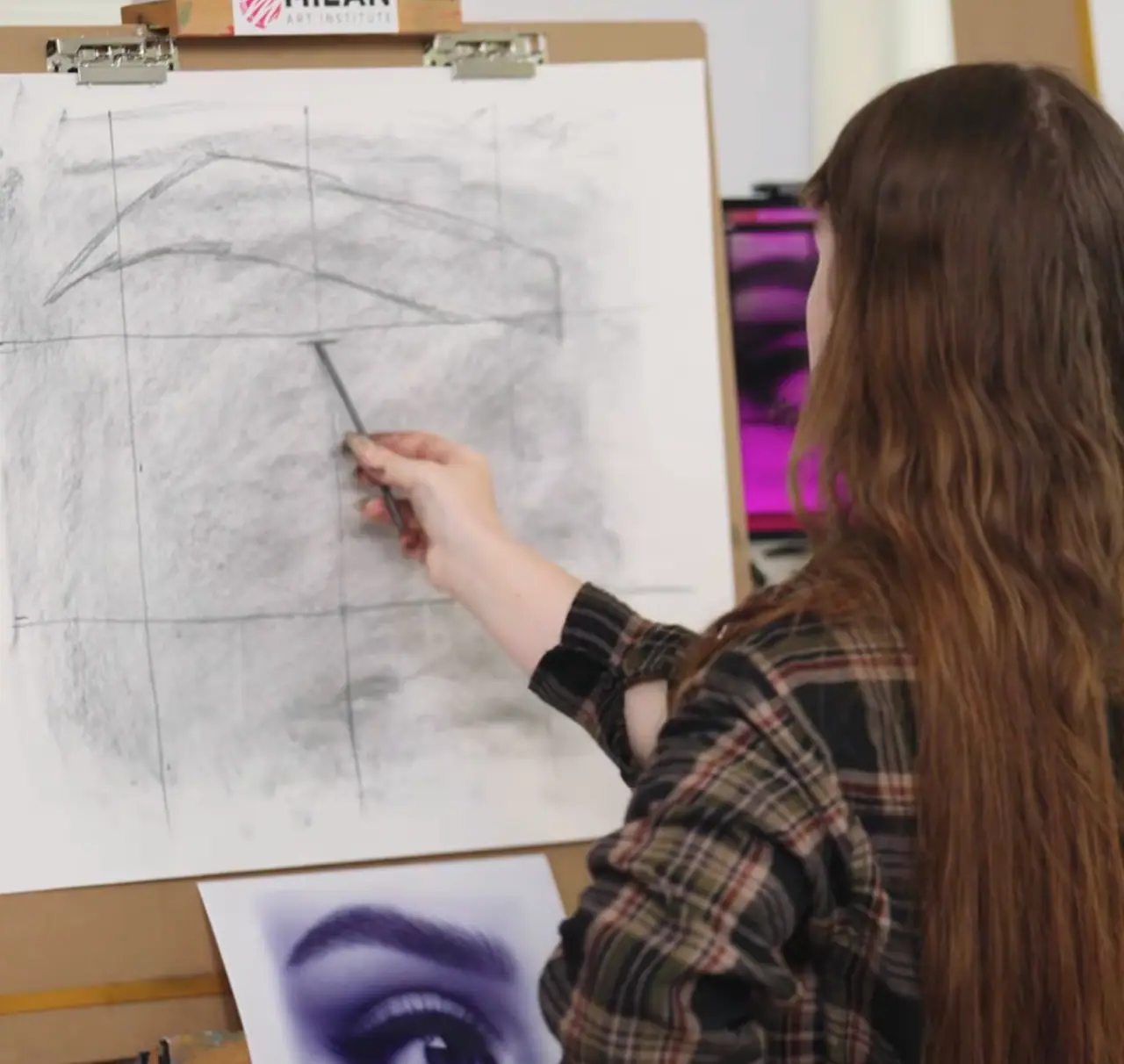 Artist with brown hair focused on drawing an eye at a wooden easel