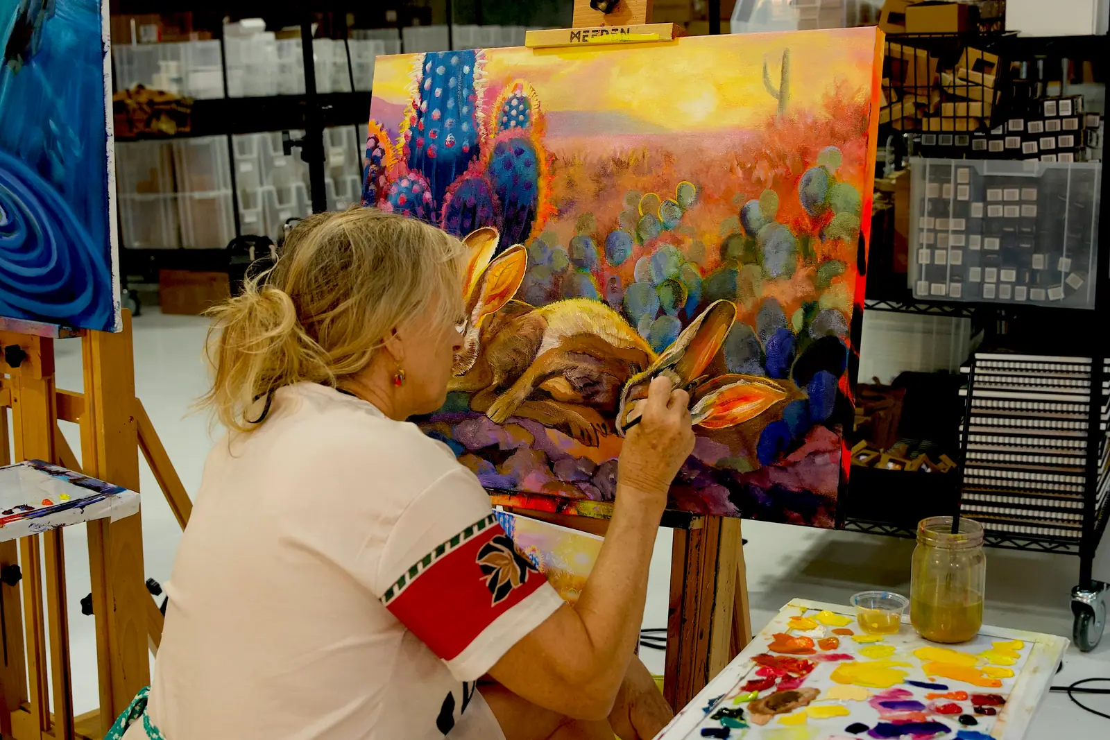 Artist painting a desert scene with a blue cactus and a brown rabbit