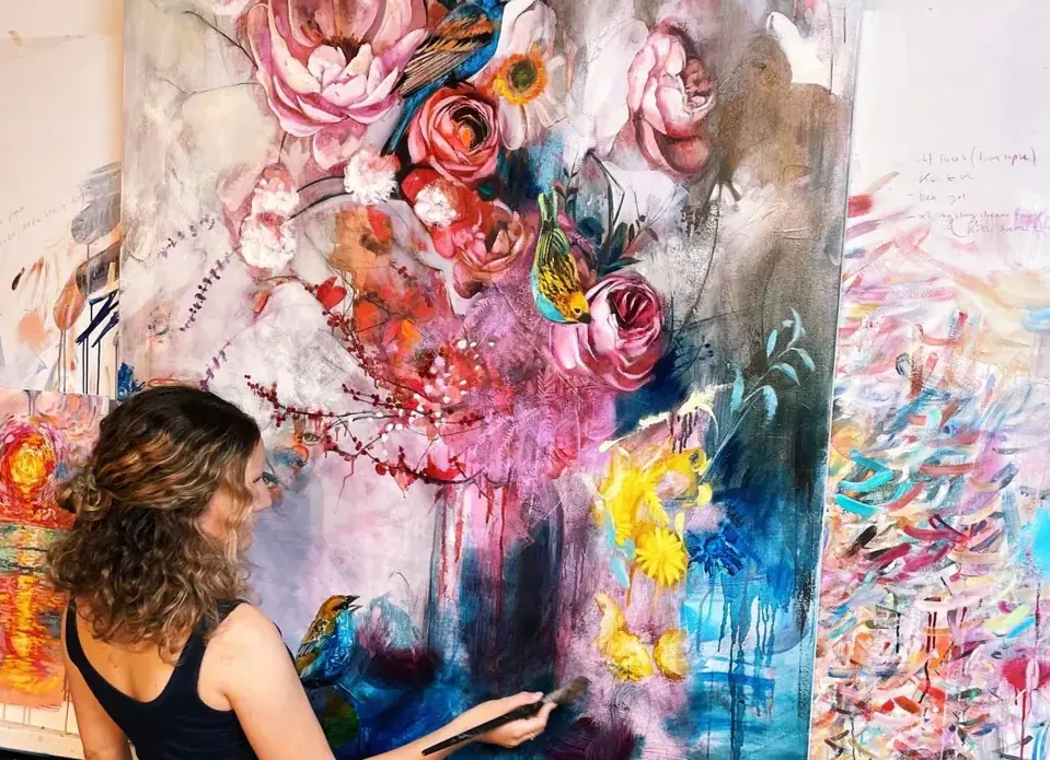 Artist painting bold pink, yellow, and blue flowers on a large canvas