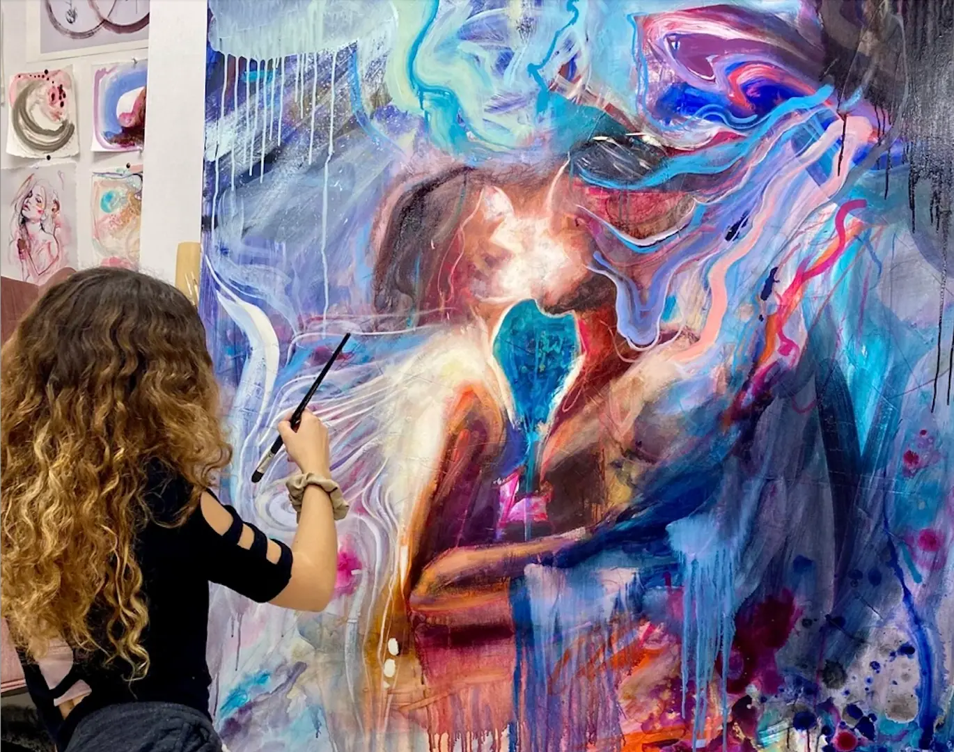 Artist at an easel painting two figures embracing surrounded by a blue and pink glow