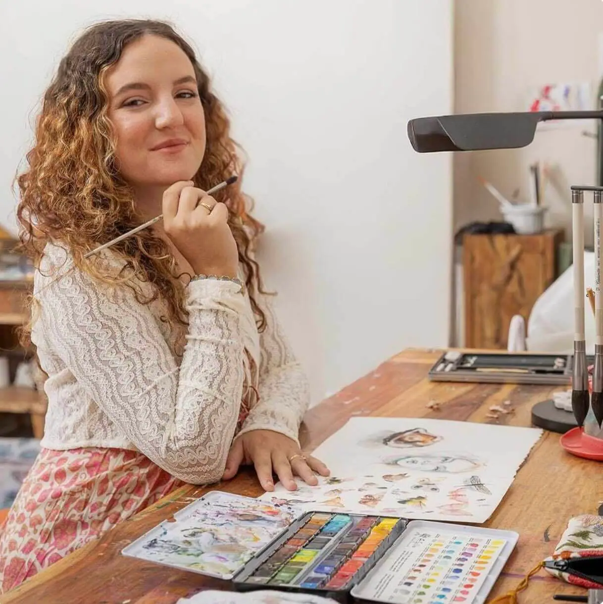 Artist seated at a table painting with watercolors and a brush in hand