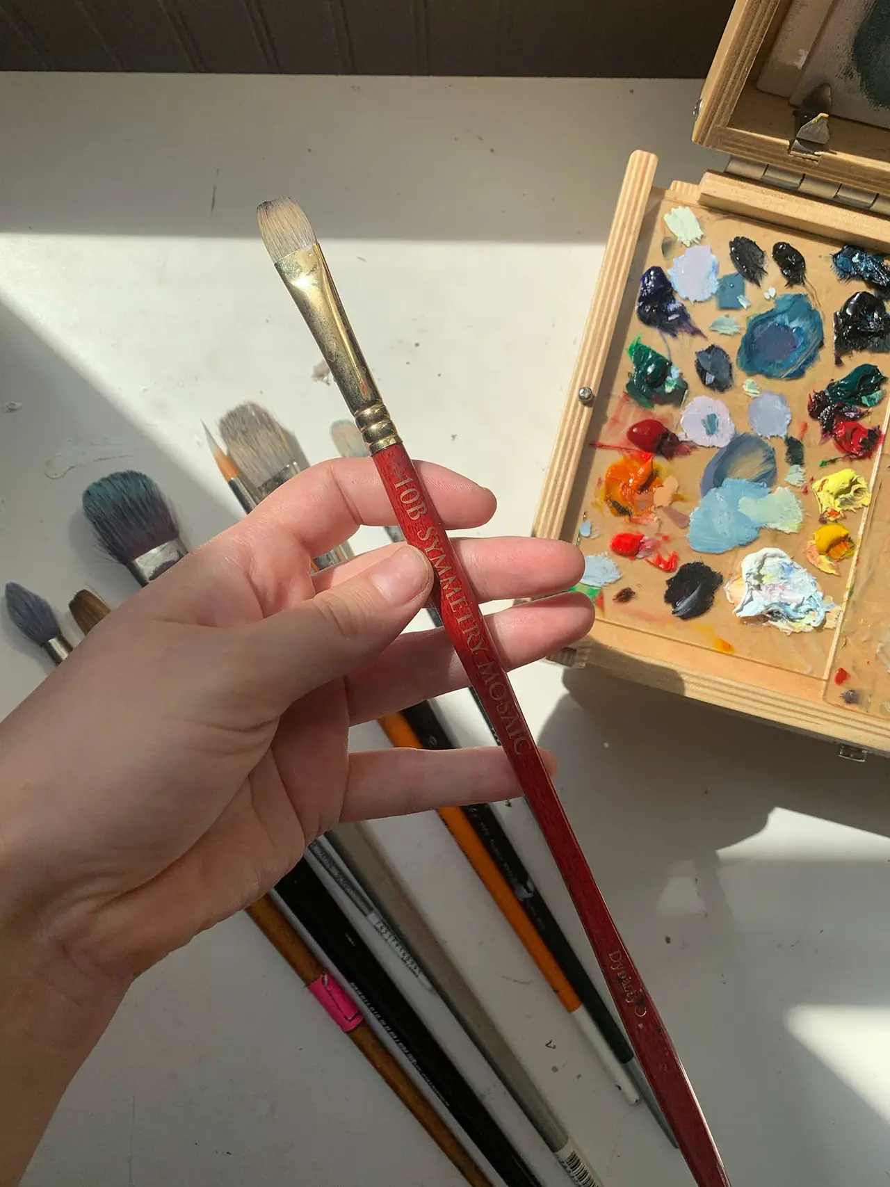 A hand holding an artist brush with an orange handle