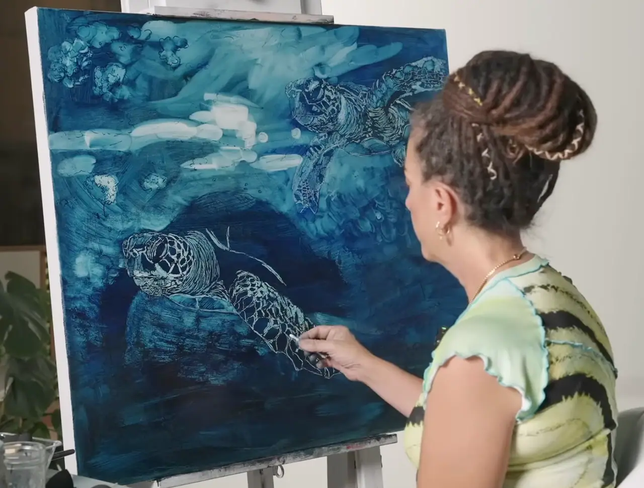 Artist subtracting highlights from sea turtles painted in blue oil