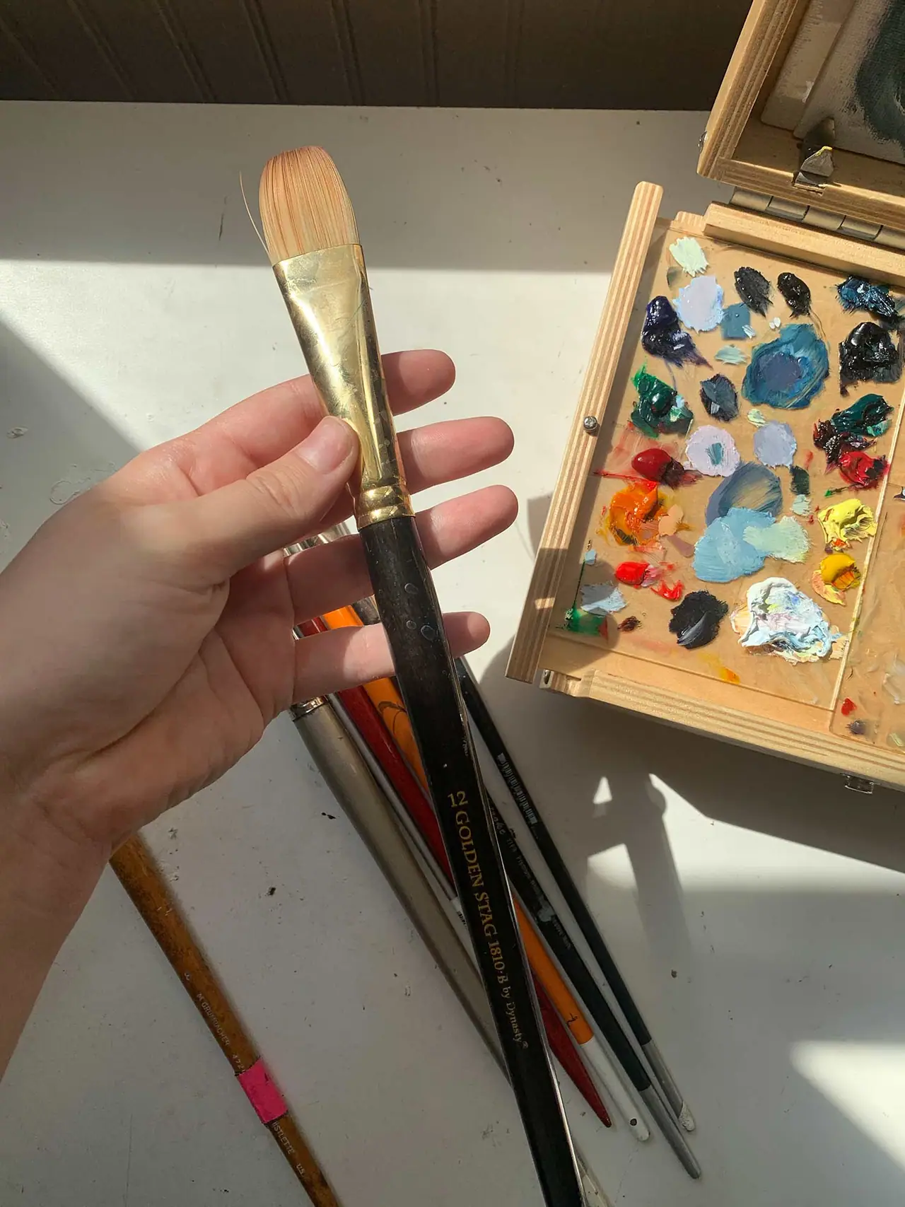 A hand holding an artist brush with a black handle
