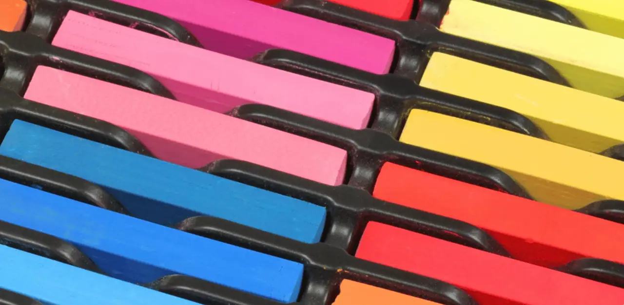 Soft pastel sticks in blue, pink, red, and yellow arranged on a tray