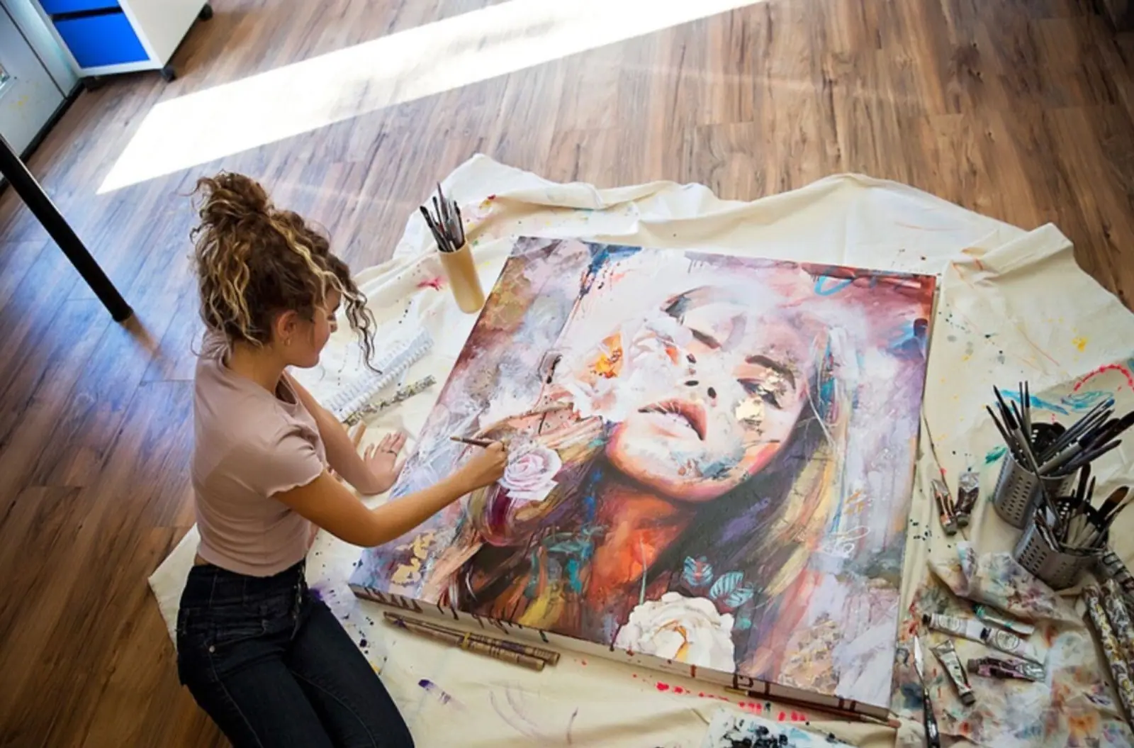 Artist kneeling on the floor painting a portrait on canvas