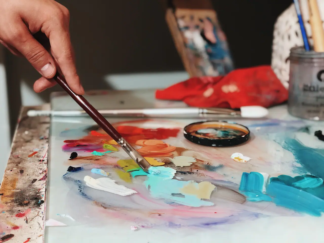 Close up of a hand loading a brush from a palette of mixed oil colors