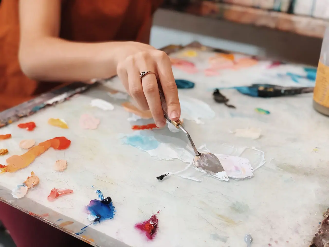 Artist mixing thick acrylic paint with a palette knife on a glass palette