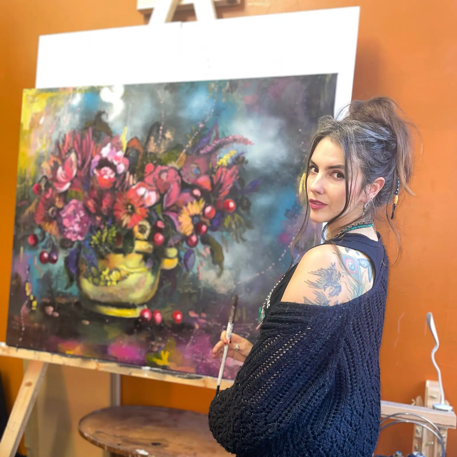 Lisa Cunningham in a black sweater standing in front of a canvas with a pink and red vase of flowers