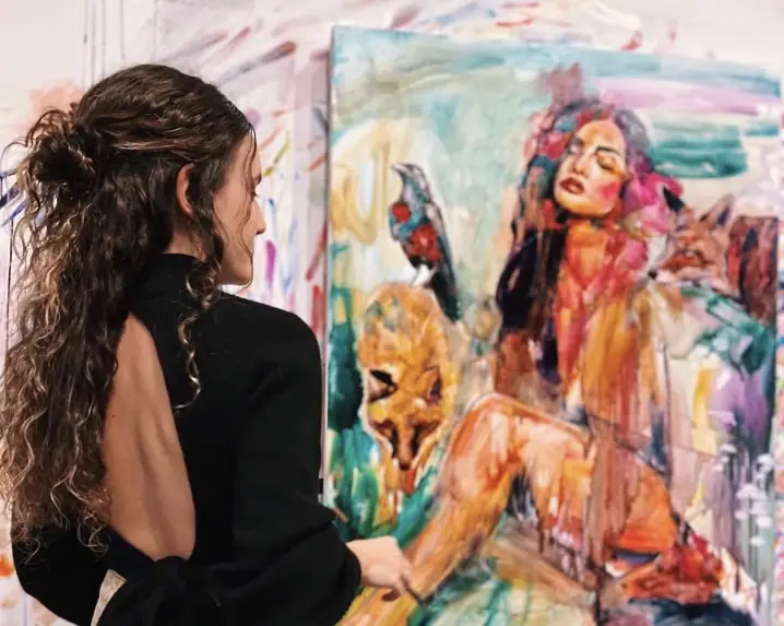 Artist in a black dress painting a figure in orange, teal, and purple