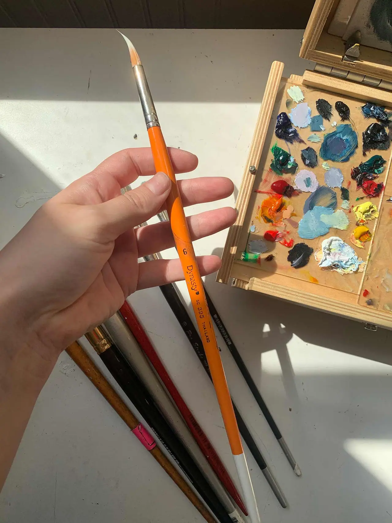 A hand holding a size 6 round artist paint brush
