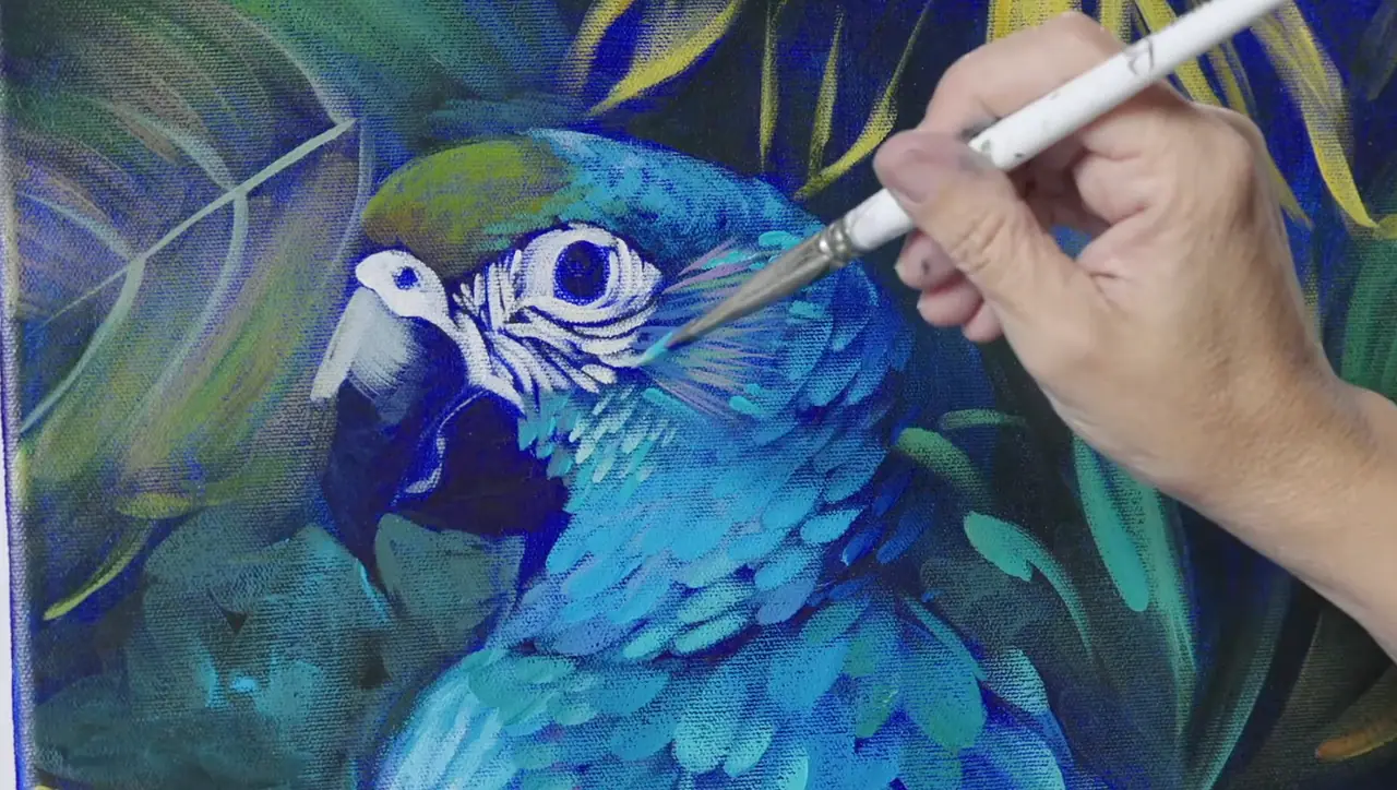 Hand using a paintbrush to paint a bird in blue and green