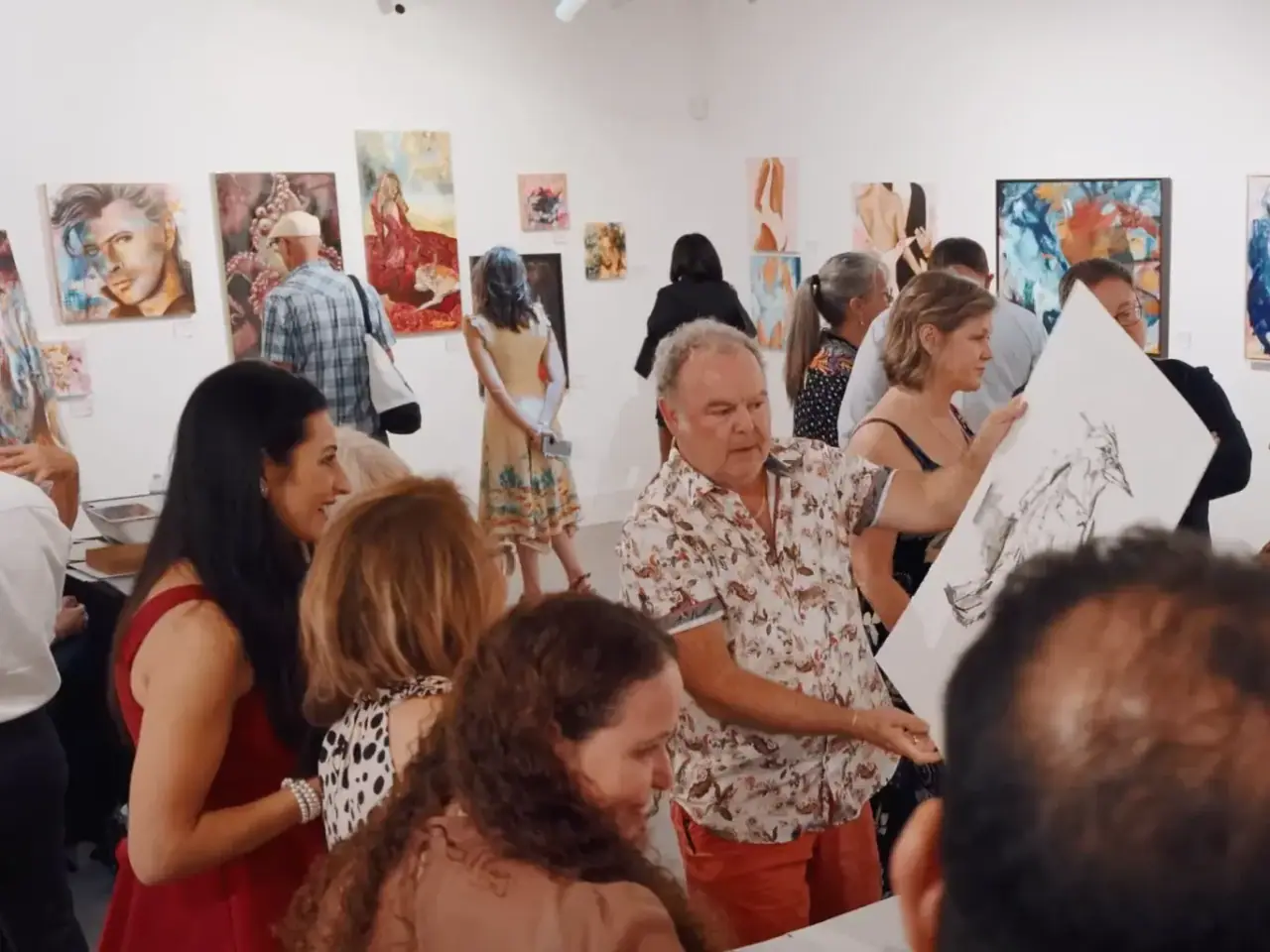 People walking through a bright gallery space lined with framed paintings