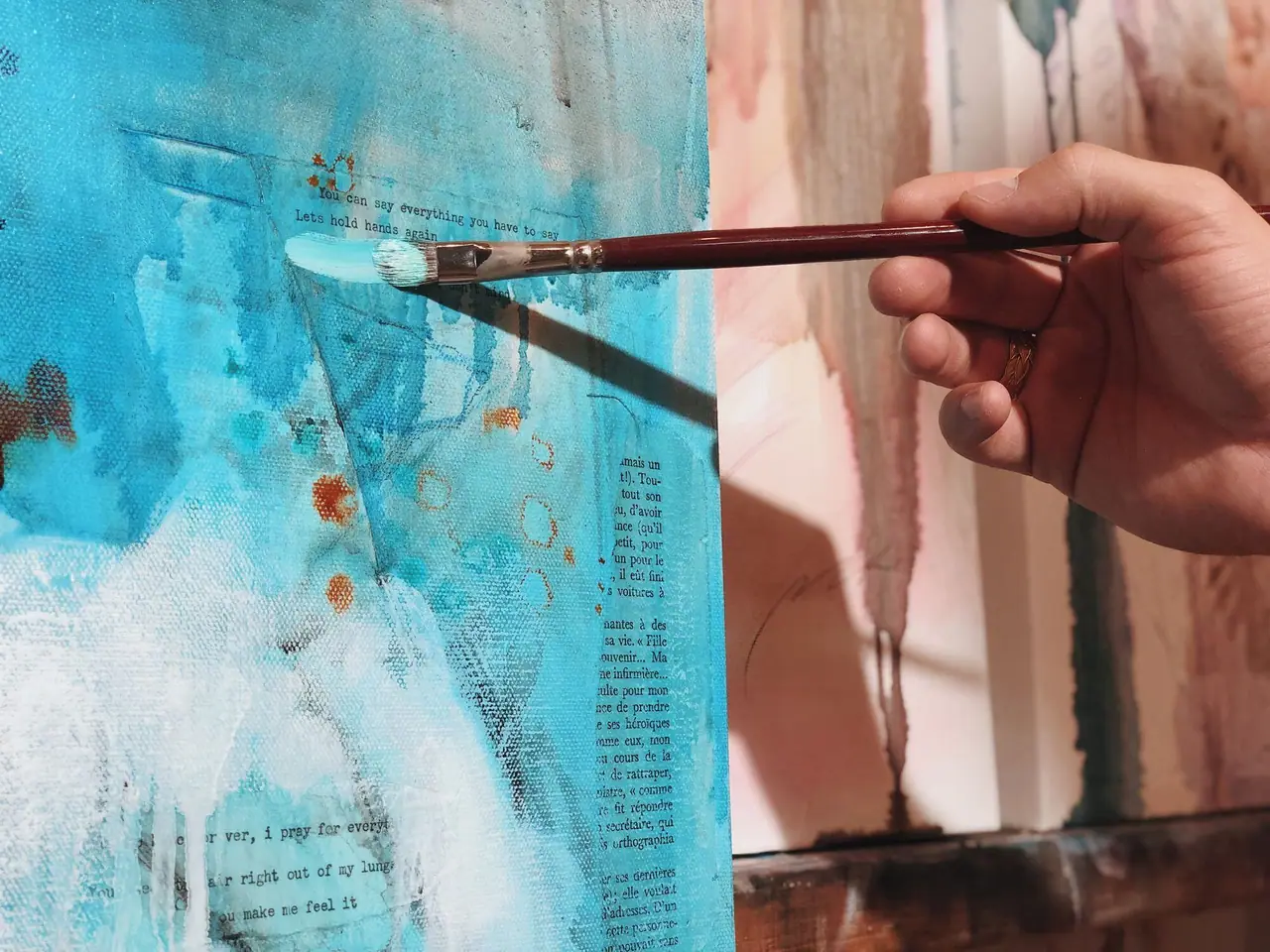 Flat brush pulling blue acrylic paint across a mixed media painting