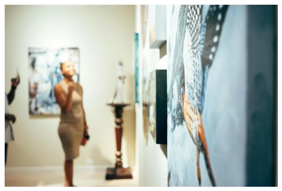 Woman standing in a gallery looking at framed paintings on a white wall