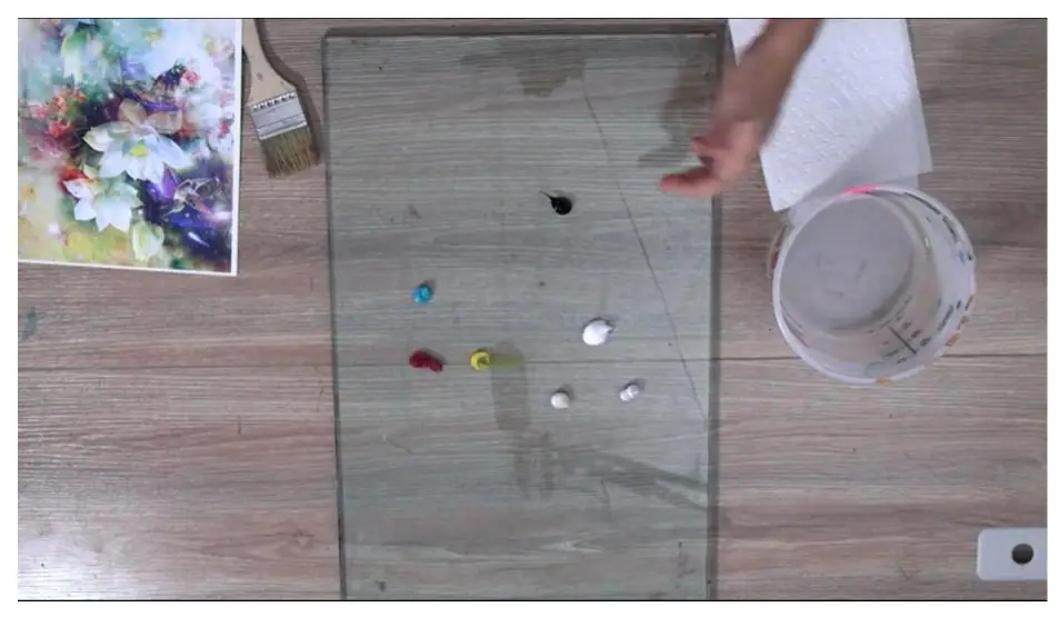 Artist palette loaded with paint beside a water bucket and brushes