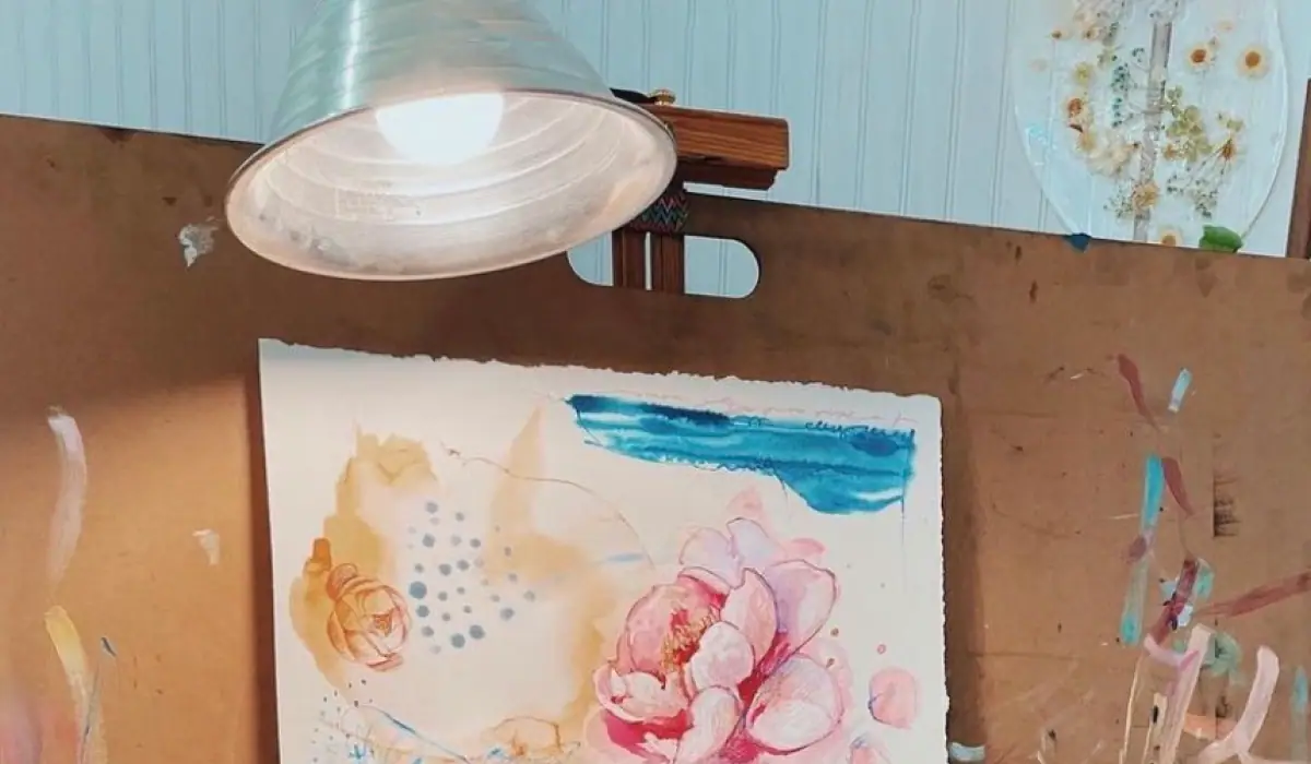 A clamp light mounted above a paper painting on a table, casting even illumination across the surface