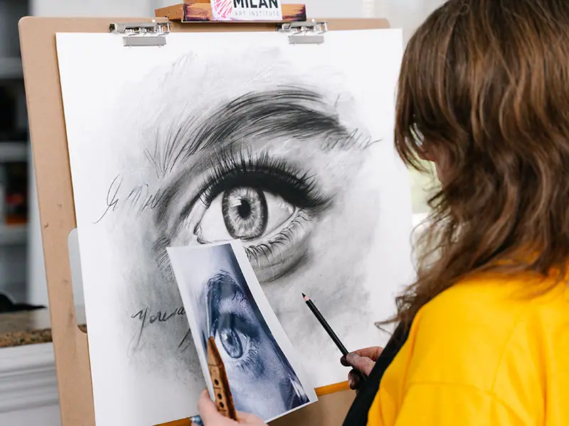 Artist in a yellow shirt drawing a detailed eye on a wooden board