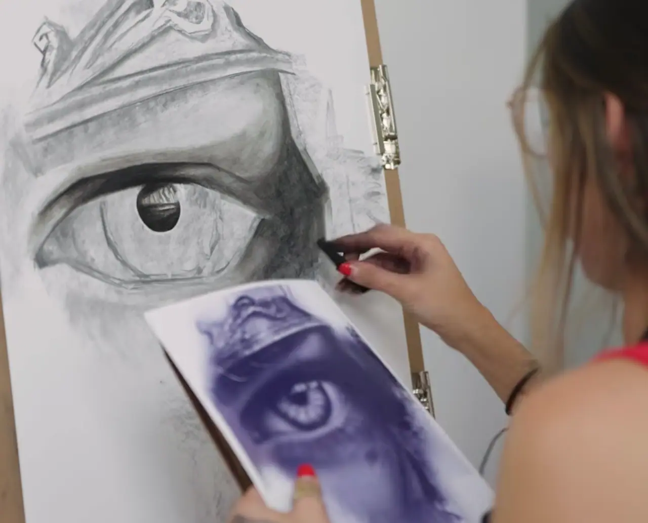 Artist drawing an eye while holding a paper reference in one hand