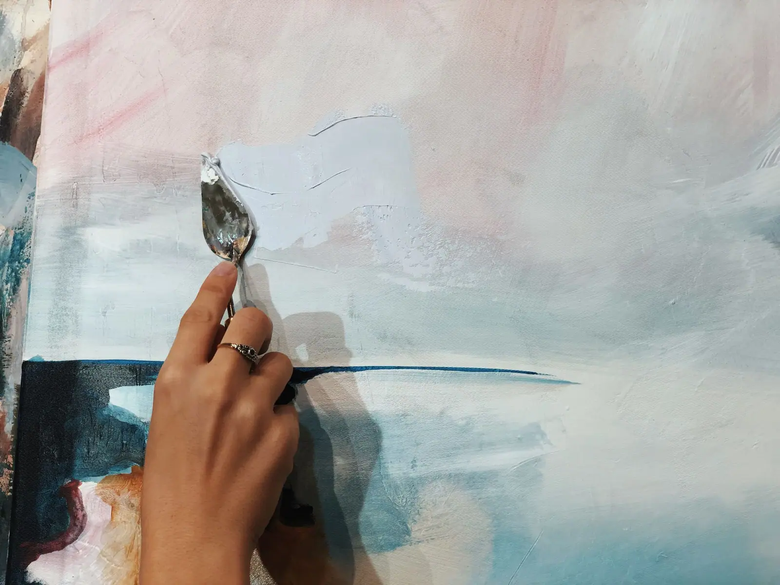 Palette knife spreading thick soft blue and pink paint on canvas
