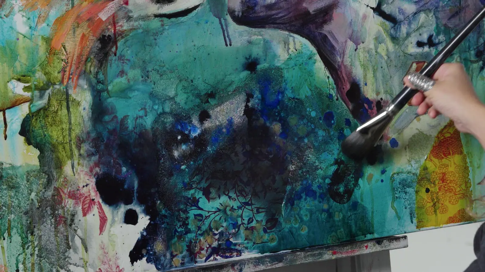 Hand holding a brush working blue and teal paint into a mixed media painting