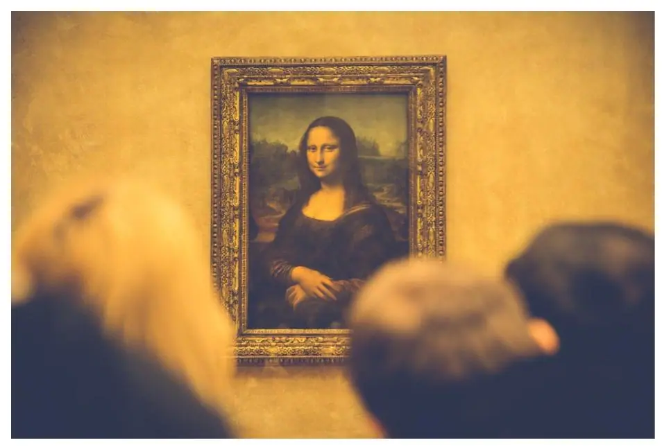 The Mona Lisa by Leonardo da Vinci on display at the Louvre, a half length portrait of a woman with a faint smile and soft shadowed modeling