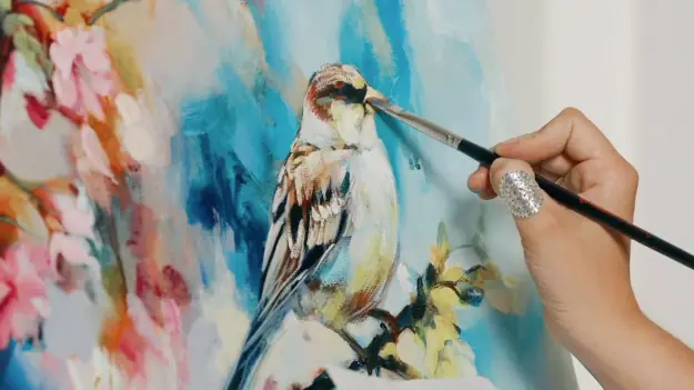 Hand painting a brown, white, and black bird on canvas with a flower background