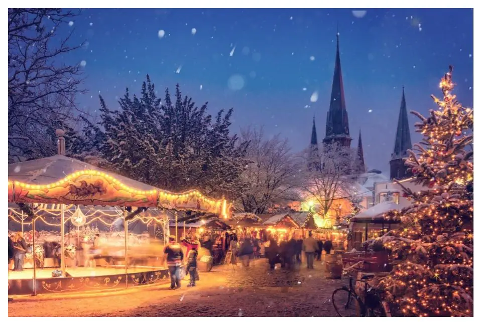 Wooden stalls at an outdoor Christmas market glowing with holiday lights at dusk