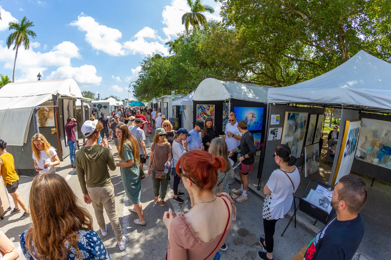 Visitors walking through an outdoor art tent show browsing paintings on display