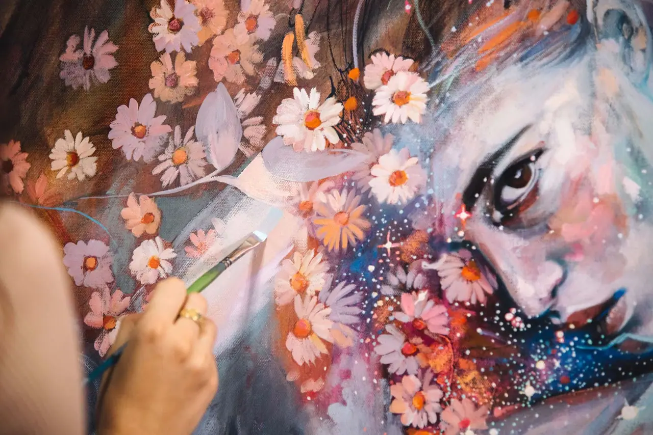 An artist painting a face with flowers, working the eye area with a small brush