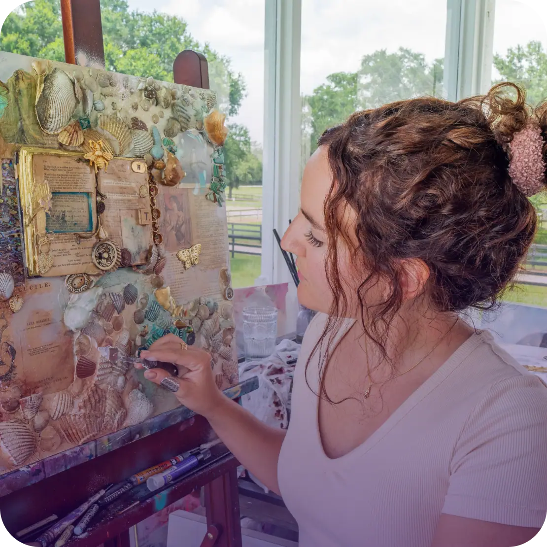 Artist seated in front of a canvas working on a shell and assemblage collage
