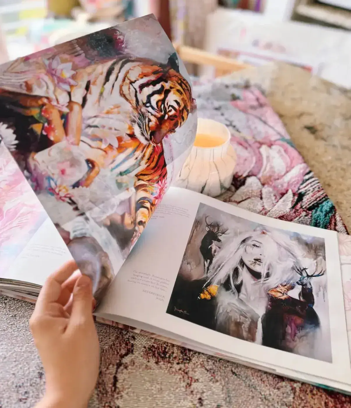 A printed art book open to a gold-toned portrait and a tiger painting, an example of a physical portfolio catalog an artist can leave with galleries