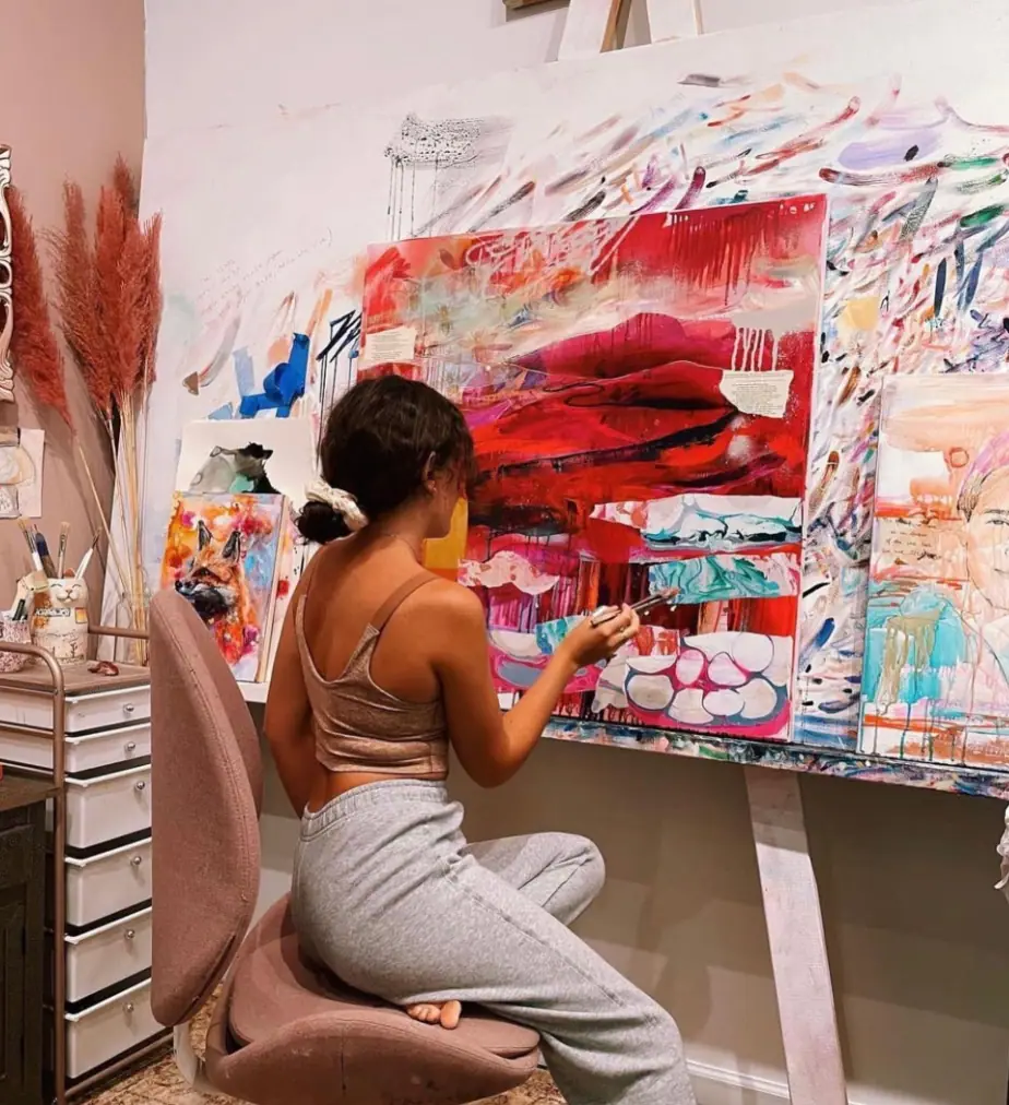 Artist seated at a canvas painting an abstract landscape during a focused studio session