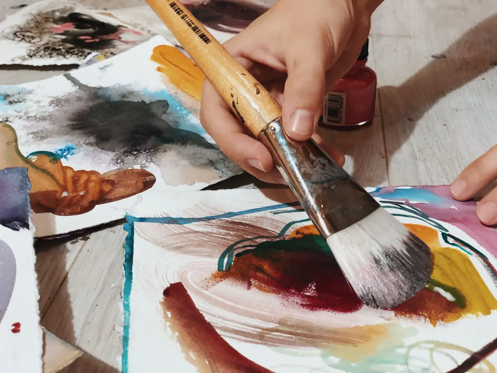 Artist covering paper with brown acrylic paint using a large flat brush