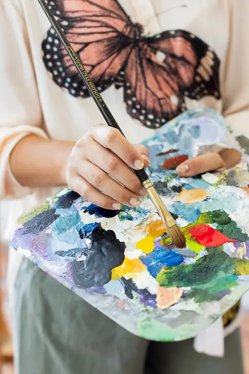 Artist holding a wooden paint palette loaded with blue, green, and red paint