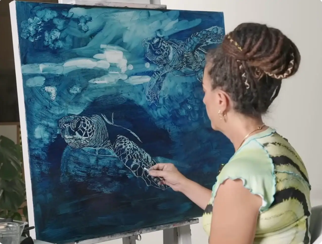 Artist blocking in a thin blue underpainting of turtles on canvas
