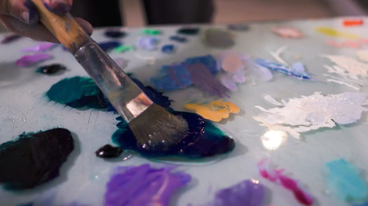 Brush mixing purple, blue, and white paint on a palette for a glaze