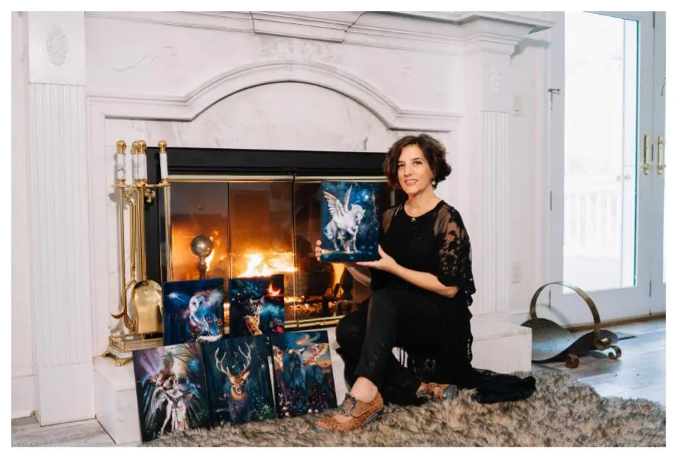 Elli Milan seated beside several of her large colorful paintings in her studio